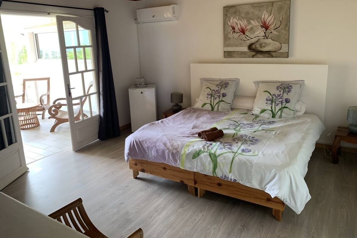 Un dormitorio con una cama de madera, un ventanal grande y un cuadro en la pared.