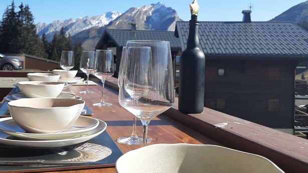 Mesa dispuesta con cuencos, copas de vino y una botella, con vistas a una cordillera.