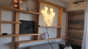 Una sala de estar moderna con un sofá gris, estanterías de madera, un letrero de neón con forma de ciervo y una imagen enmarcada de un ciervo.
