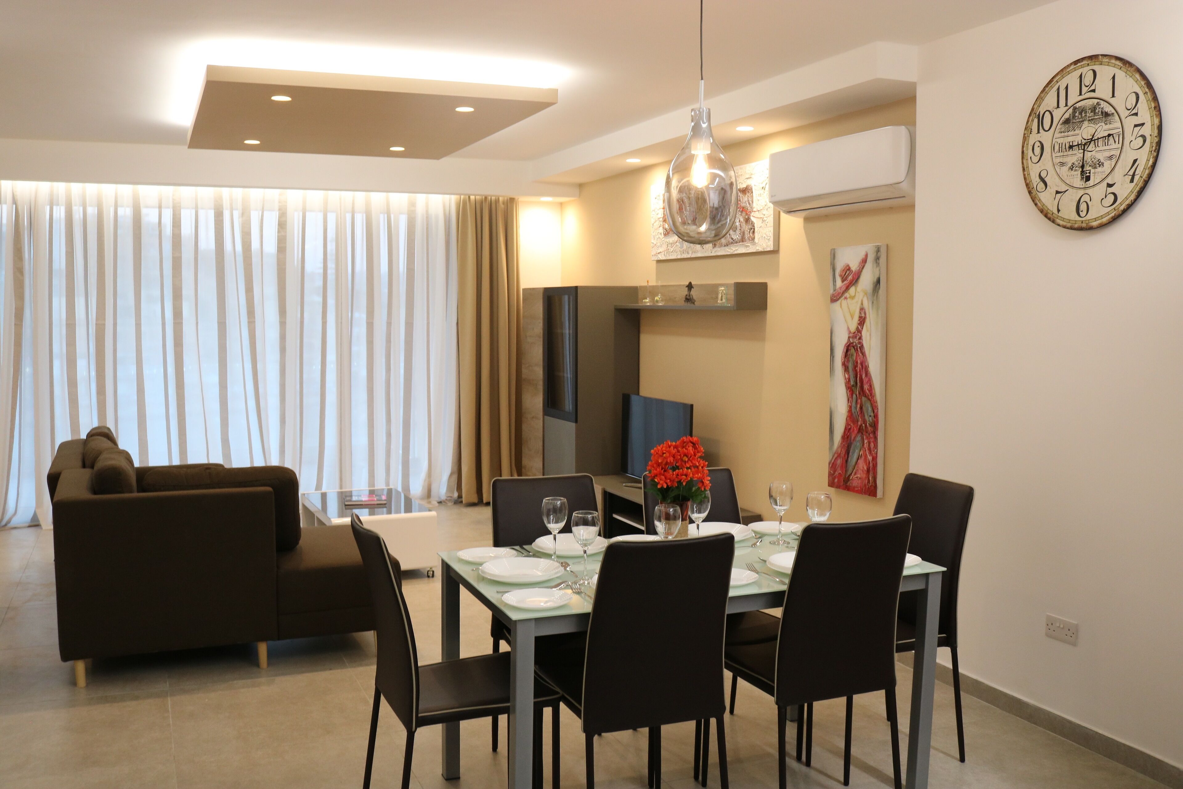 Un espace repas moderne avec une table dressée pour quatre personnes, un canapé et une grande horloge murale.