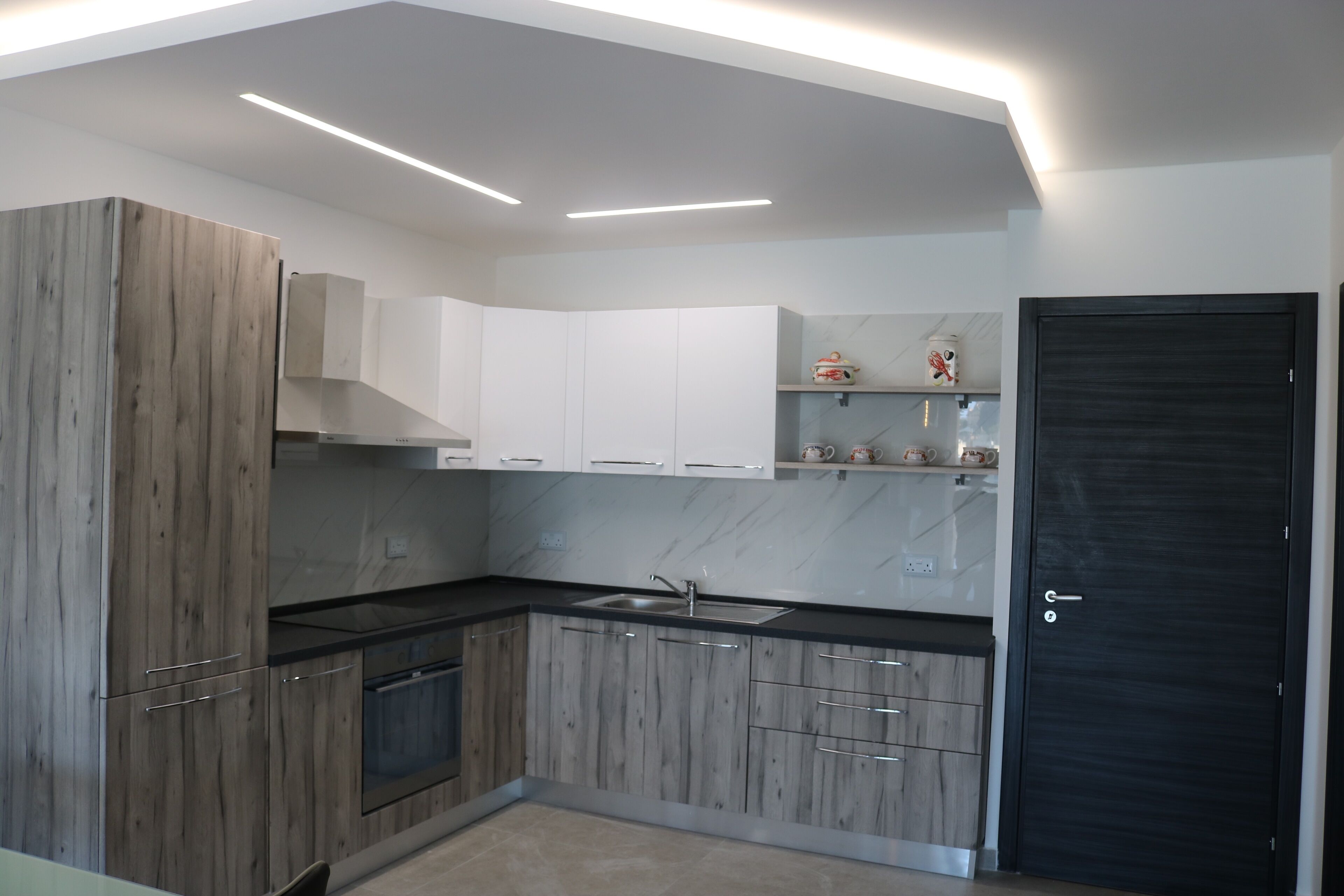 Une cuisine moderne avec des meubles en bois, un plan de travail noir et une porte noire.