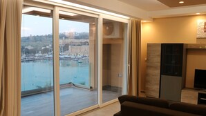 Ein modernes Wohnzimmer mit einem großen Schiebeglasfenster, das auf einen Balkon mit Blick auf einen Jachthafen führt.