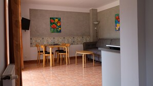 A dining area with a table and chairs, a sofa, and a TV mounted on the wall. - 3 room apartment with terrace, 450m from the sandy beach, close to the nature park, garden (Rowy)