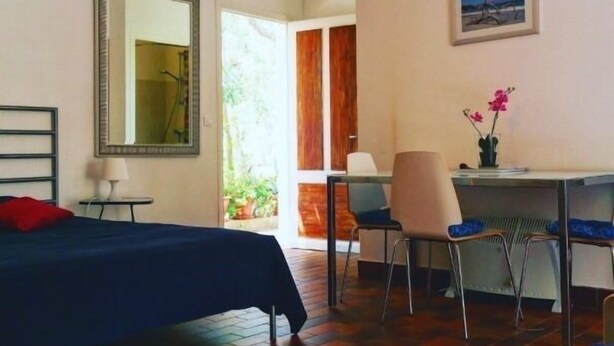 A hotel room with a bed, a desk, a chair, a mirror, and a door leading to an outdoor area. - Studio & large garden 200m Calvi beach (Calvi)