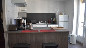 A modern kitchen with a central island, two bar stools, a stainless steel refrigerator, and a window providing natural light. - DUPLEX OF 110 M2 NEAR QUAY AND SHOPS, 8 persons (Port-Vendres)