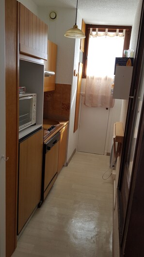 Compact kitchen with oven, tile floor, and small window.