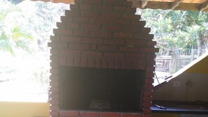 A brick-built outdoor oven with a tiled floor, a trash bin, and a yellow wall in the background. - Six lakes site in the Juquitiba region (Dos Barnabés)