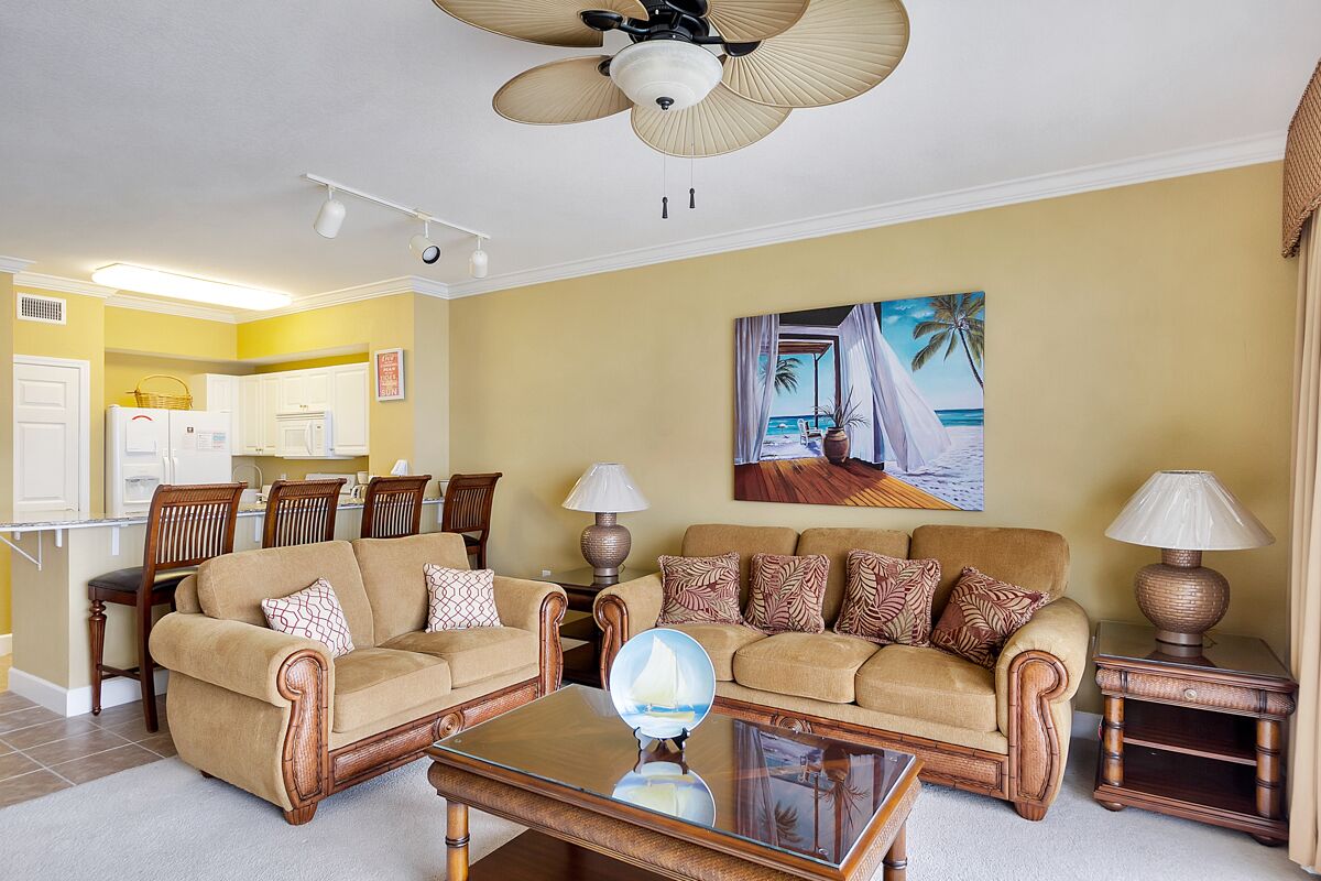 A living room with two sofas, a coffee table, and a ceiling fan. There is a painting of a beach scene on the wall.