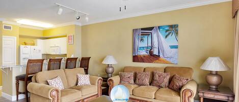 A living room with two sofas, a coffee table, and a ceiling fan. There is a painting of a beach scene on the wall.