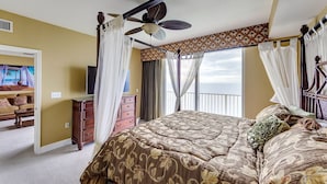 A bedroom with a large bed, a ceiling fan, a TV, and a view of the ocean.
