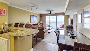 A hotel room with a kitchen, dining area, and a balcony with a view.