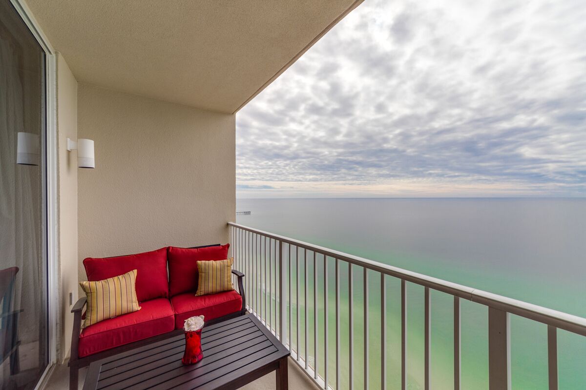 Ein Balkon mit einer roten Couch, einem kleinen Tisch und Blick aufs Meer.