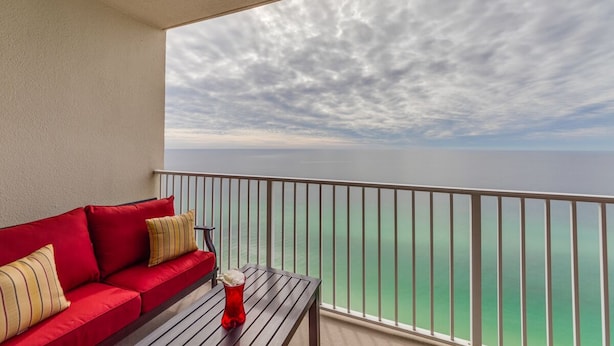 A balcony with a red sofa and a table, overlooking a body of water.