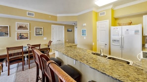 A kitchen with granite countertops, wooden chairs, a dining table, and white appliances.