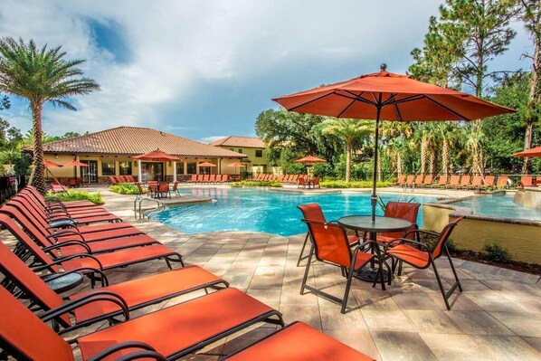 A poolside area with lounge chairs and umbrellas, a pool, and a building with a tiled roof.