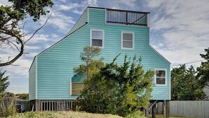 A two-story house with a steep gable roof, a front porch, and a wooden fence. - Family Affair oceanfront private pool Pet Friendly  (Salvo)