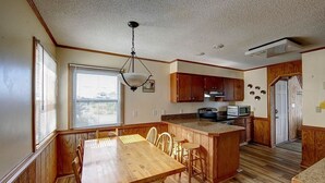 A kitchen with wooden cabinets, a dining table with chairs, a built-in island, and a window with blinds. - Family Affair oceanfront private pool Pet Friendly  (Salvo)