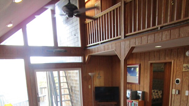 A spacious living room with a high ceiling, wooden walls, a large window, and a balcony. - Family Affair oceanfront private pool Pet Friendly  (Salvo)