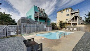 A backyard with a swimming pool, a barbecue grill, and two multi-story buildings with balconies. - Family Affair oceanfront private pool Pet Friendly  (Salvo)