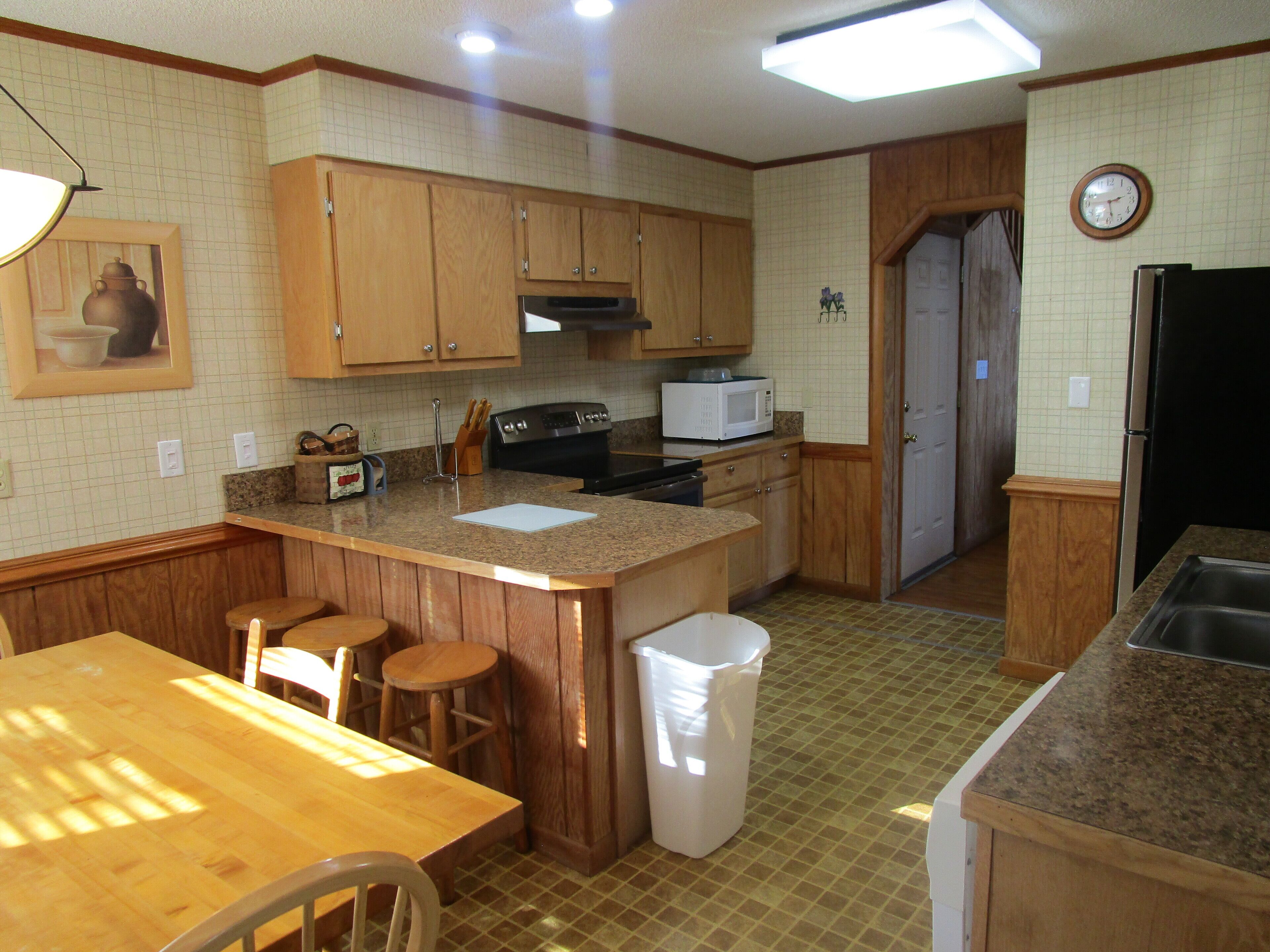 A kitchen with wooden cabinets, a microwave, a sink, and a dining area with a table and chairs.