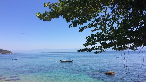 A calm sea with a boat and rocky shore. - Camping do Bené (Angra dos Reis)