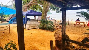 A beachside area with tents, a wooden table, and a bench. - Camping do Bené (Angra dos Reis)