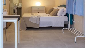 Une chambre à coucher comprenant un lit, une table de chevet, un portant à vêtements et un luminaire fixé au plafond.