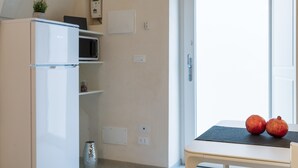 Une cuisine compacte équipée d’un réfrigérateur, d’un four à micro-ondes et d’une petite étagère sur laquelle est posée une plante en pot.