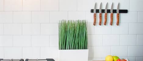 A kitchen with a gas stove, a potted plant, a knife rack, and a cutting board with tomatoes and lemons.