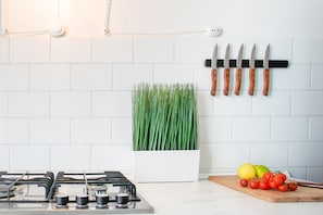 Una cocina con estufa a gas, una planta en maceta, un colgador para cuchillos y una tabla de cortar con tomates y limones.