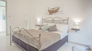 A bedroom with a metal-framed bed, two bedside tables with lamps, a bench, and a painting of a boat on the wall.