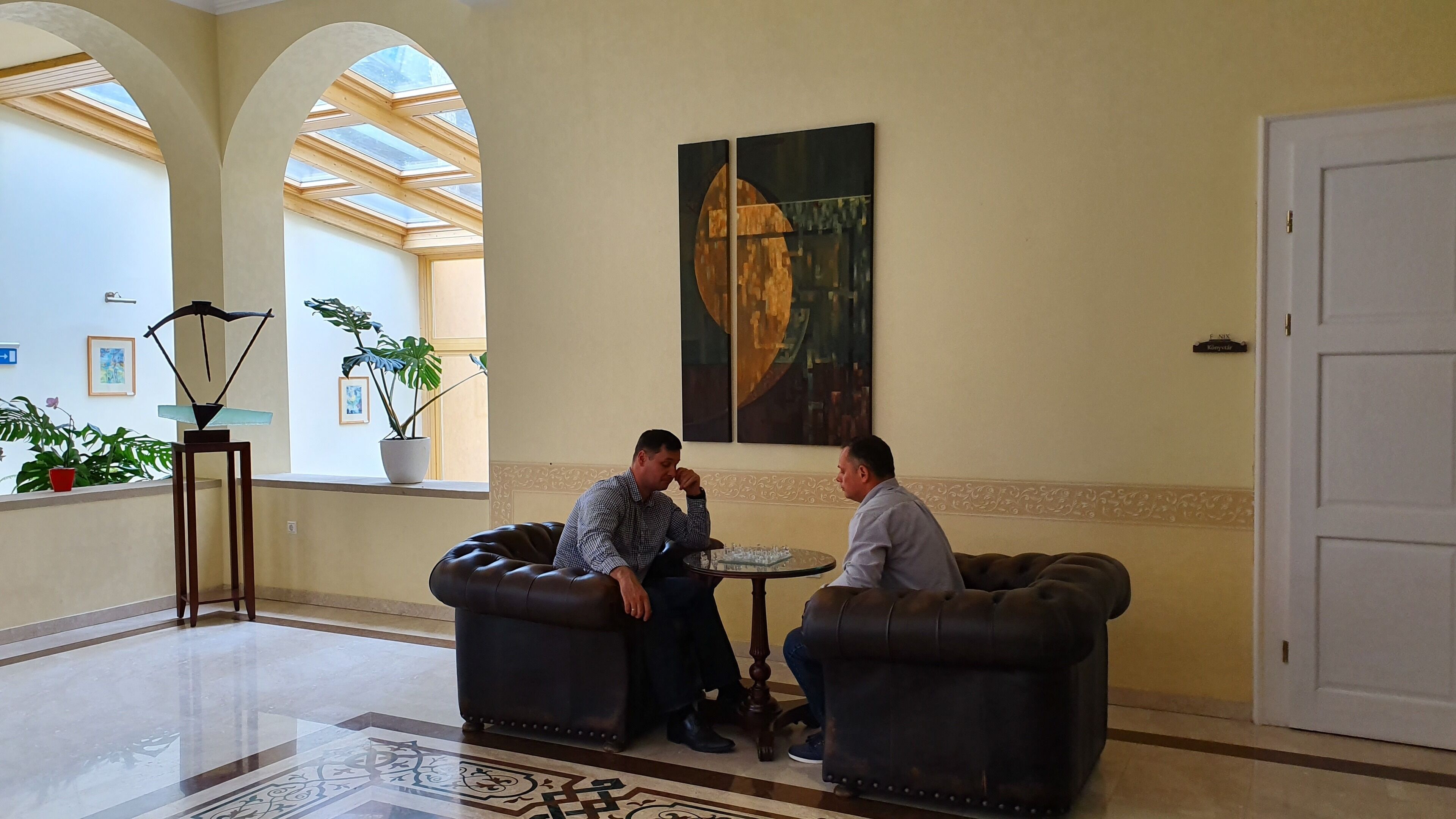 Eine Lobby mit zwei Ledersofas, einem Schachbrett und einem großen abstrakten Gemälde an der Wand.