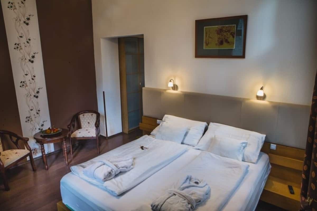 A hotel room with two beds, a sitting area with a chair and table, and a wall-mounted artwork.