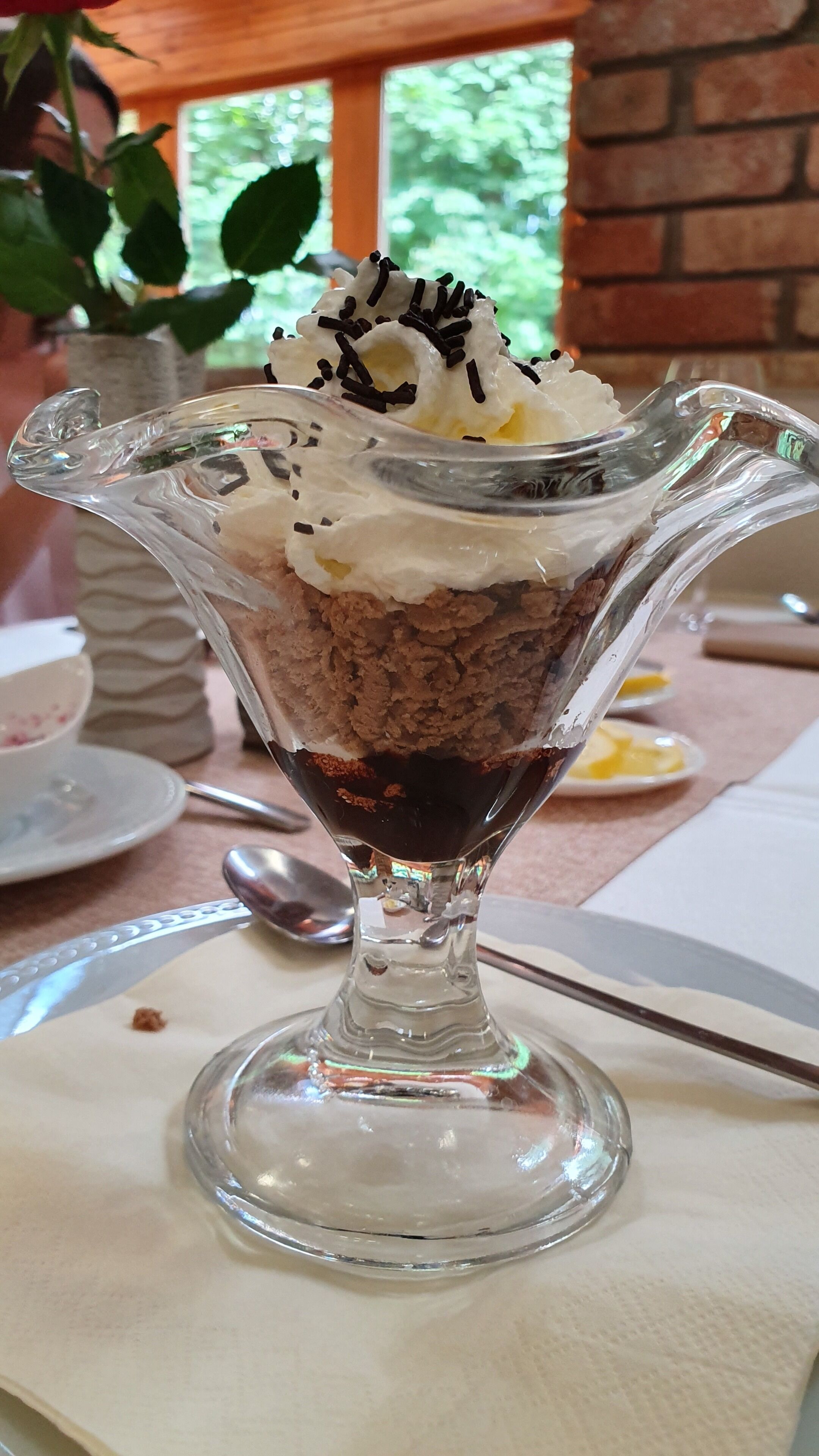 A dessert in a glass bowl with whipped cream and chocolate on a table.