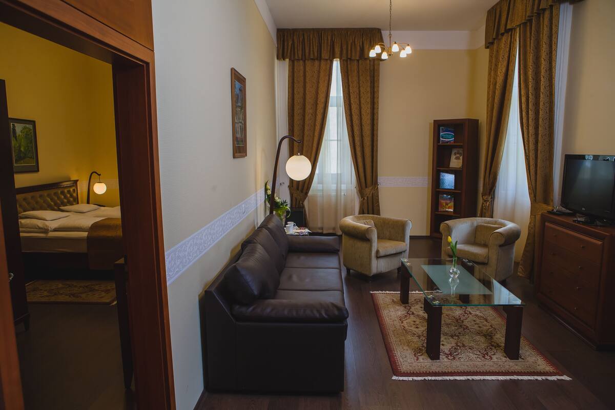A living room with a sofa, armchairs, a glass coffee table, a television, and a bookshelf.