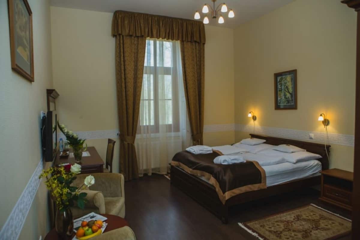 A hotel room with a bed, a desk with a chair, a vase with flowers, and a window with curtains.