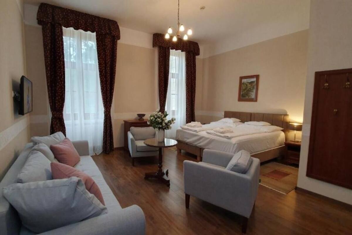 A hotel room with a sofa, two armchairs, a small table with a vase, a bed, and a nightstand.