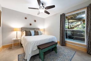 A bedroom with a bed, a bench, a standing lamp, a ceiling fan, and a window with curtains.