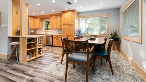 Una cocina moderna con armarios de madera, un comedor con mesa y sillas, y un ventanal con persianas.