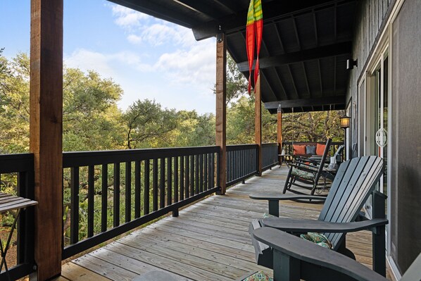 A wooden deck with outdoor seating, a railing, and a view of trees and sky.