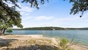 Vista de un lago con playa arenosa, árboles y una colina distante.