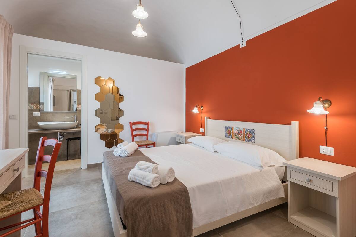 A bedroom with a bed, bedside tables, a chair, a desk, and a bathroom visible through an open door.