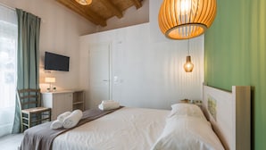 Una habitación de hotel con cama, escritorio, silla, televisor y ventana con cortinas.