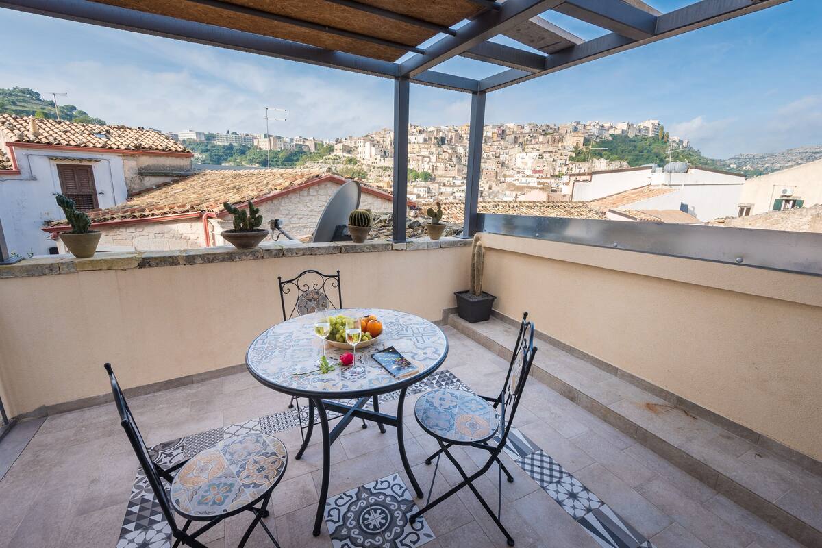 A rooftop terrace with a round table, two chairs, and potted plants.