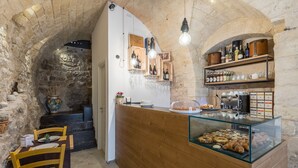 Un interior rústico con un arco de piedra, mostrador de madera con vitrina y una zona de estar con sillas.