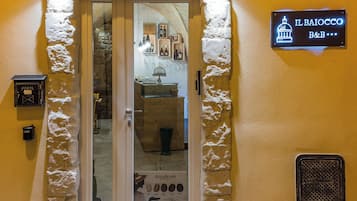 A hotel entrance with a glass door, a sign above indicating the name 'IL BAIOCCO B&B', and a display case with wine bottles inside.