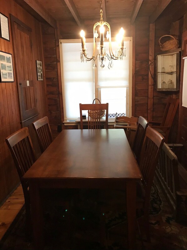 A wooden dining room with a large table and chairs, a chandelier, and a window with blinds.