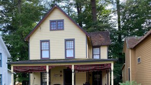 A two-story house with a porch, a front door, and a small garden area. - Victorian Summer Cottage in Historic Sacandaga Park,Northville,NY (Northville)