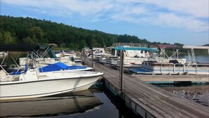 A dock with several boats moored, a wooden pier, and a forested hillside in the background. - Victorian Summer Cottage in Historic Sacandaga Park,Northville,NY (Northville)