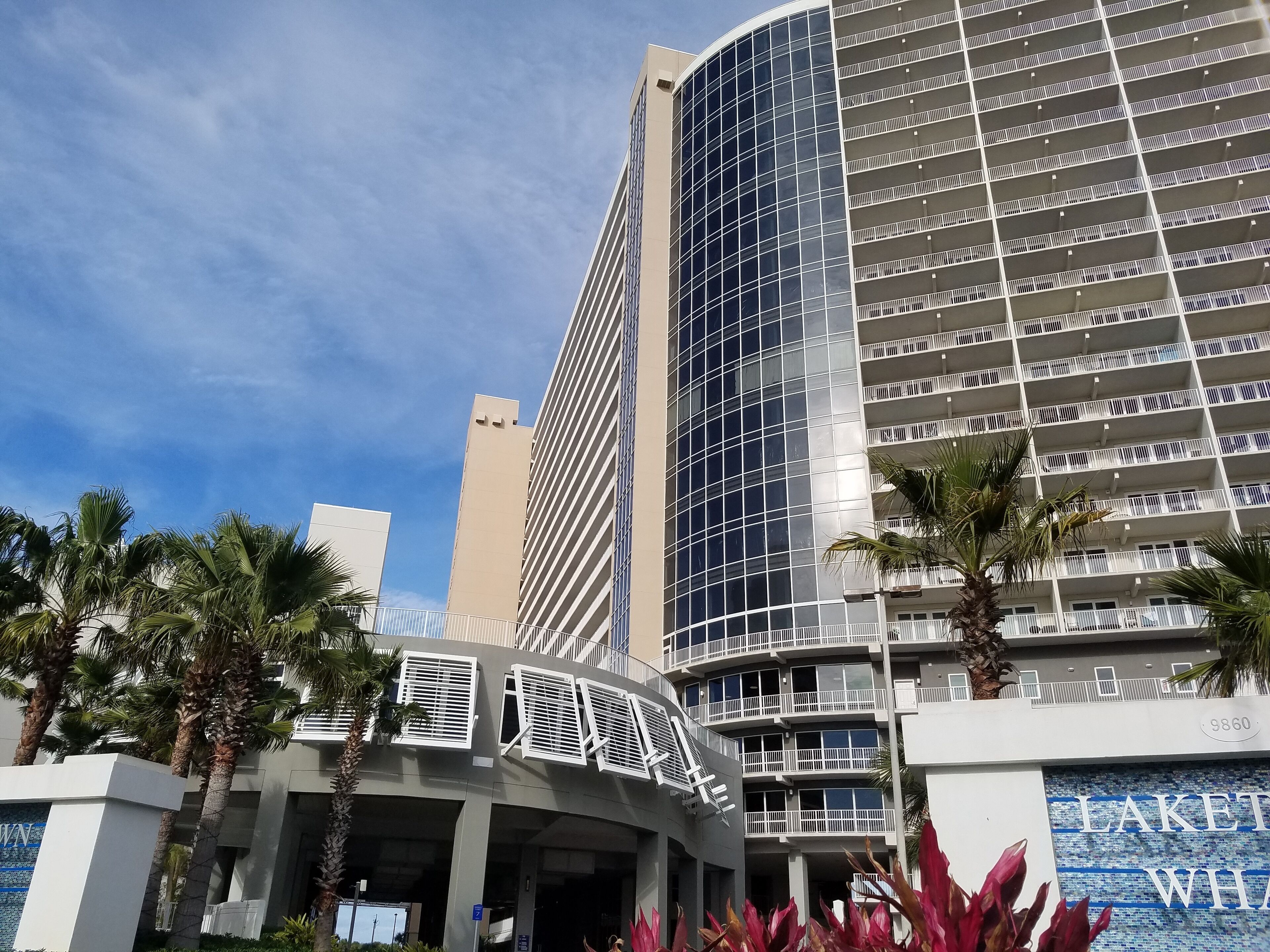 Un hotel moderno con fachada curva, varios balcones y palmeras en primer plano.